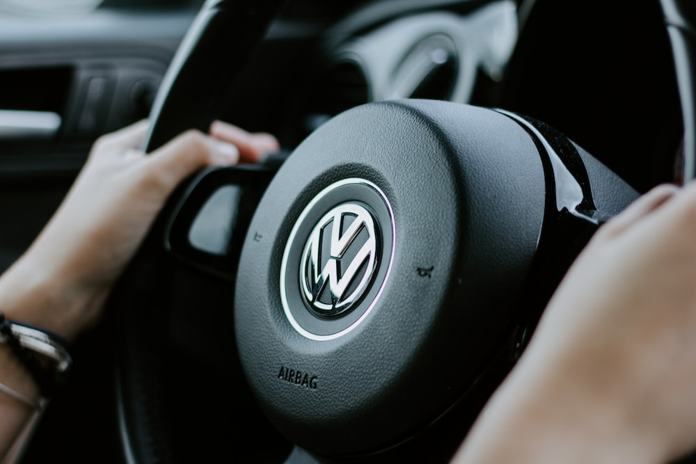 A woman's hand is holding the steering wheel of a volkswagen.