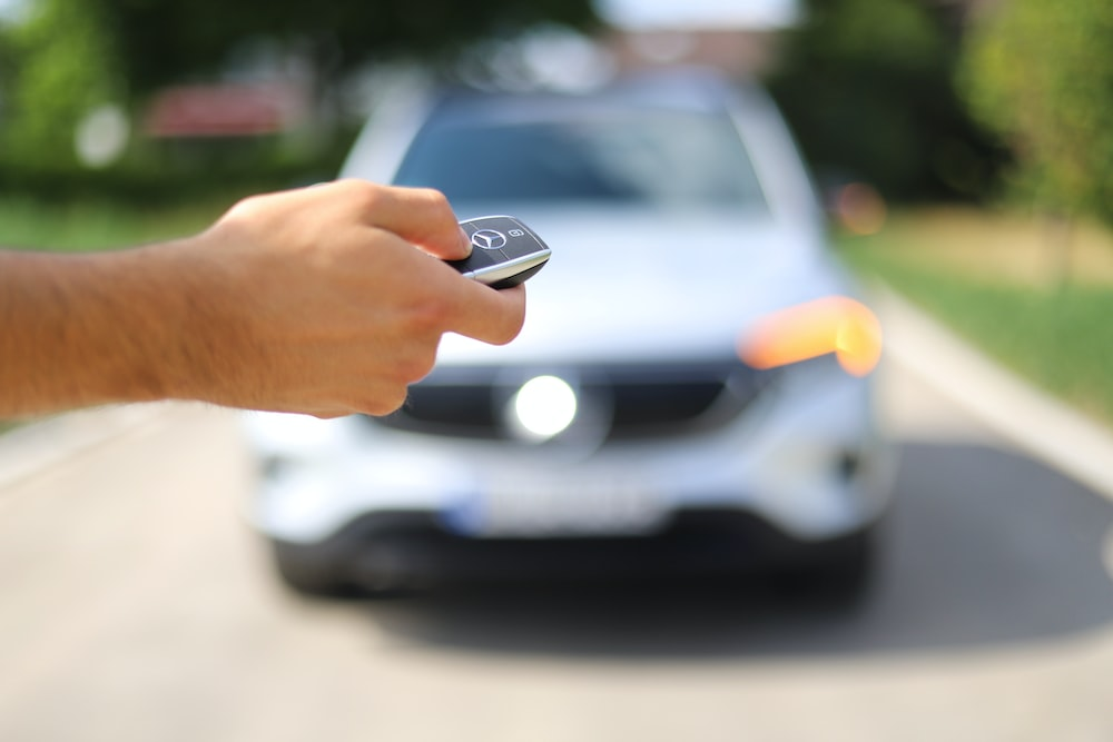 A person holding a car key in front of a car.