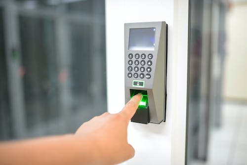 A person pressing a fingerprint reader on a door.