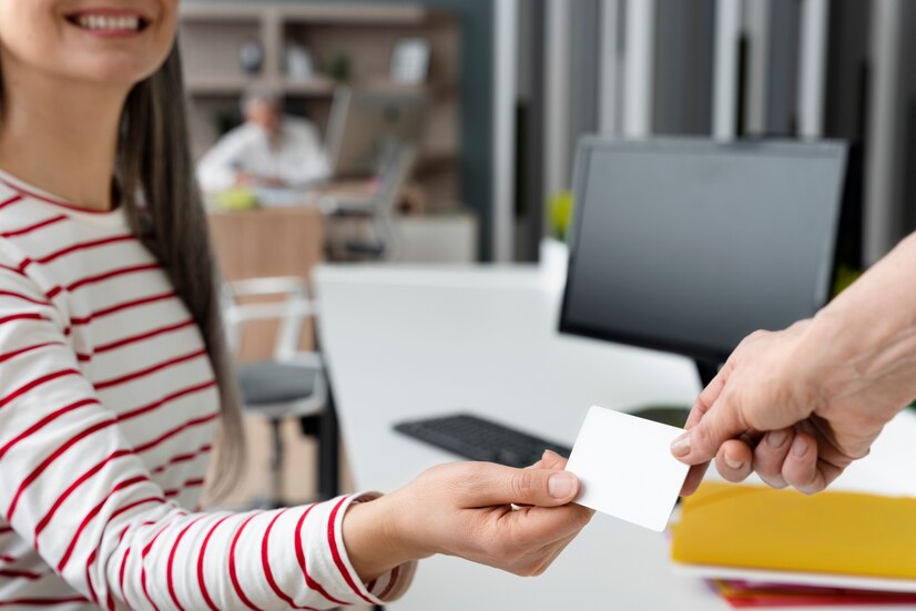 A woman handing a business card to a man in an office.
