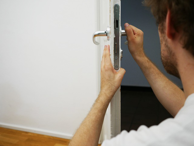 A man fixing a door handle in an empty room.
