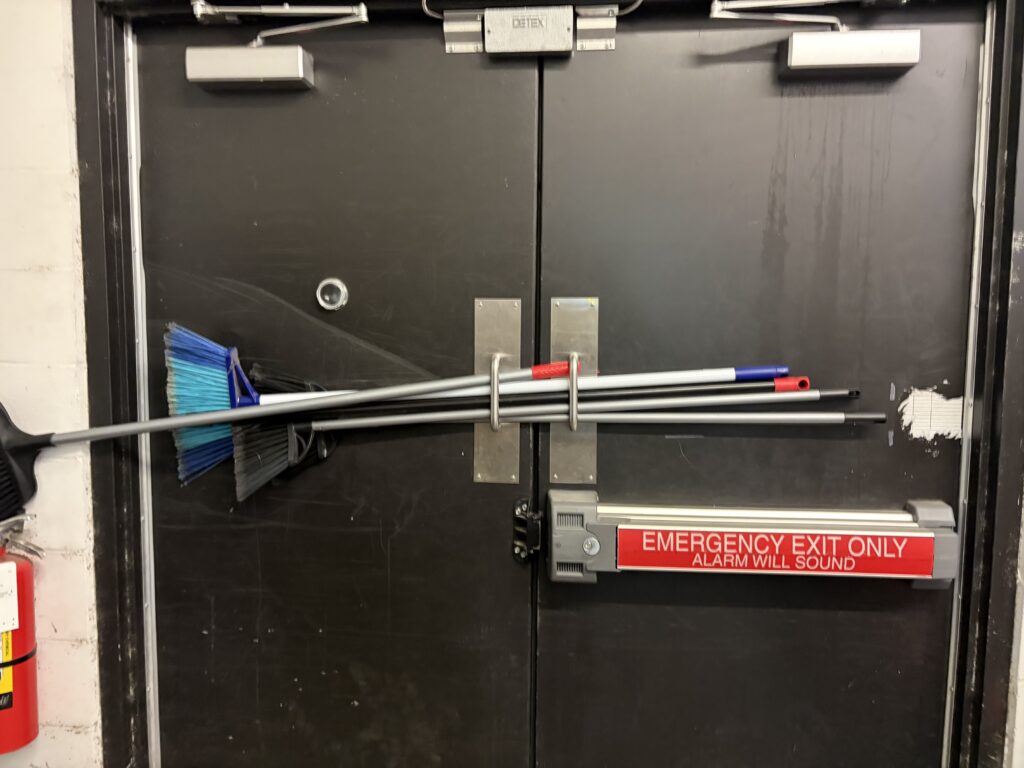 Broom wedged through emergency exit push bar as makeshift door lock - why you should call a locksmith