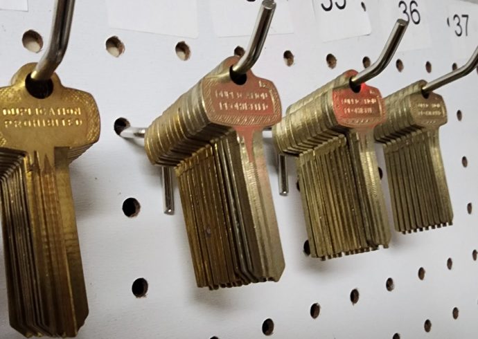 A group of brass keys hanging on a peg board.