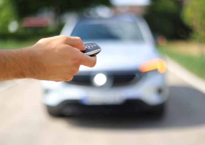 A person holding a car key in front of a car.